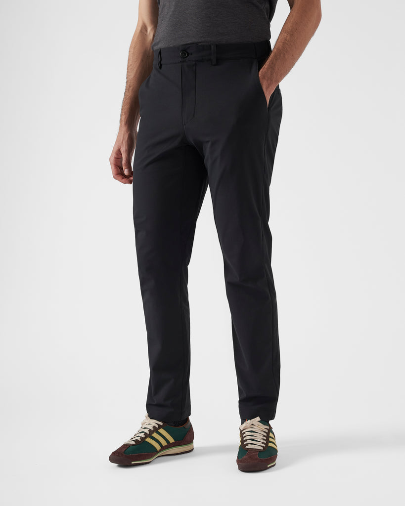 The Black Ones | Performance-Wear Brand | Lightweight Performance-Wear | Mens workwear office wear commuter cycling trousers in black. A model stands front on to the camera wearing a grey t-shirt and green, yellow and brown adidas wales bonner sneakers paired with the black trousers, with his hand in his pocket. 
