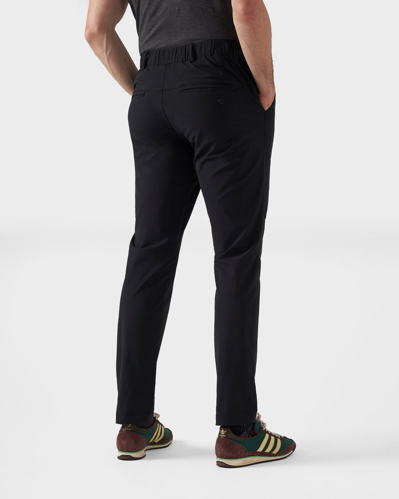 A shot of the back side of the black commuter trousers, showing the welted back pockets. The trousers are paired with green, yellow and brown wales bonner x adidas sneakers and a grey t-shirt.