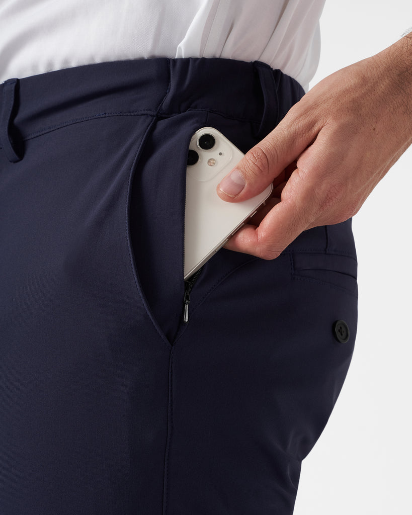 Hand sliding a mobile phone into a front zippered pocket to illustrate size and depth of pockets.